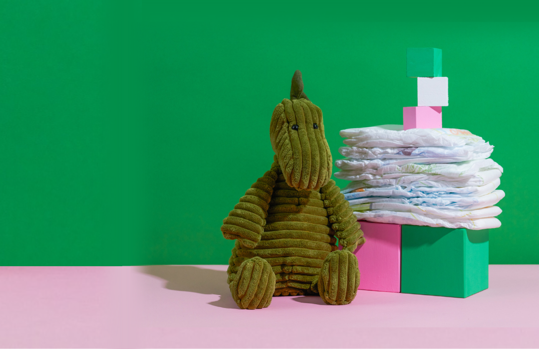 Stack of diapers on blocks with dinosaur stuffed animal on bright green background
